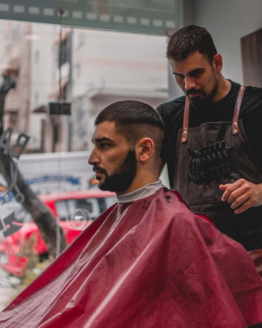 Άντρας με φρεσκοκουρεμένο skin fade και περιποιημένη γενειάδα, προφίλ, με μπορντό μπέρτα