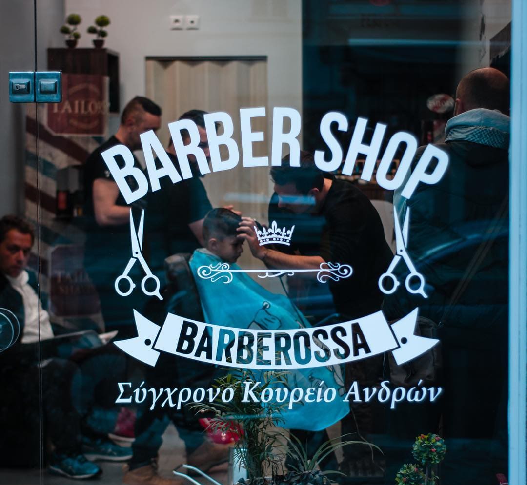 Η βιτρίνα του Barberossa με το σήμα του καταστήματος στο τζάμι και το κουρείο γεμάτο πίσω της